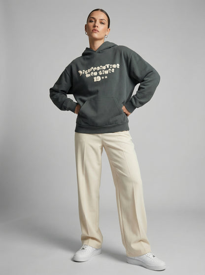 Person wearing a dark gray hoodie with text "Disappointing Men Since 19**", beige pants, and white shoes on a gray background